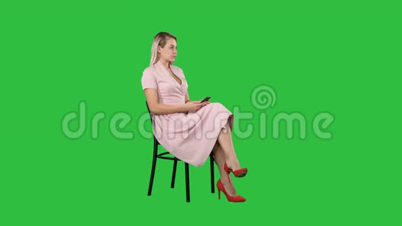 穿着粉红色连衣裙的女人坐在椅子上在绿色屏幕上等人Chroma键视频的预览图