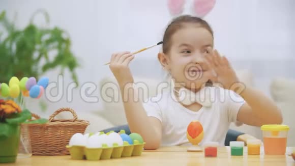小顽皮的女孩头上戴着兔子耳朵选择了红色来画一个鸡蛋女孩在上面画了一颗心视频的预览图