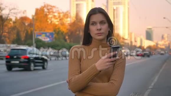 疲惫的黑发白种人女孩紧张地站在路边手里拿着电话的肖像视频的预览图