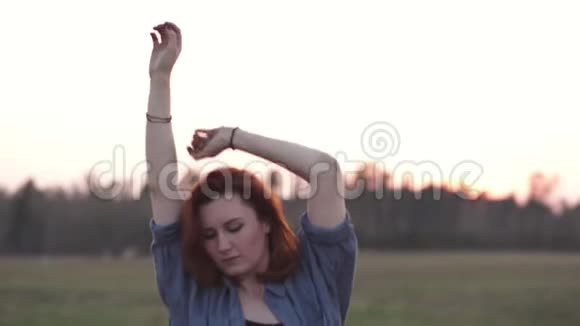 日落时分一位身穿蓝色牛仔裤夹克的年轻红发女郎在汽车旁靠近跳舞视频的预览图