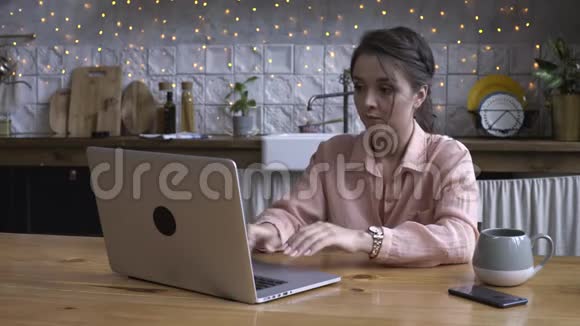 一位年轻貌美的女士坐在厨房里用笔记本电脑工作库存录像现代视频的预览图
