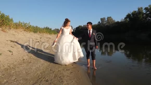 美丽的新娘穿着白色的裙子新郎赤脚在河岸边的水中行走相亲相爱的一对视频的预览图