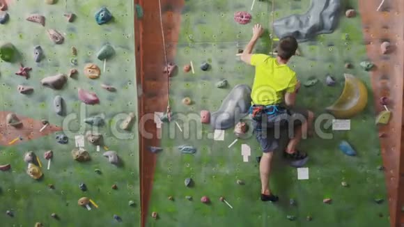 男性登山者爬上房间里的悬崖壁伸手抓住一个专业的集中登山者向上移动视频的预览图