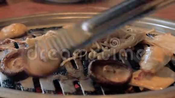 厨师在韩国烧烤盘上准备蘑菇美味的烤肉在金属烤架上烤蘑菇烧烤视频的预览图