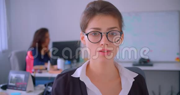 一位戴眼镜的年轻白种女商人在室内的办公室里微笑着看着摄像机的特写镜头视频的预览图