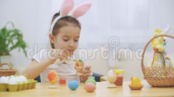 小顽皮的女孩头上戴着兔子耳朵选择了一个橙色的颜色来画一个鸡蛋女孩在嚼东西视频的预览图