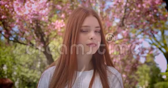 迷人的姜女学生穿着白色衬衫在粉红色的花园里梦幻地进入镜头视频的预览图