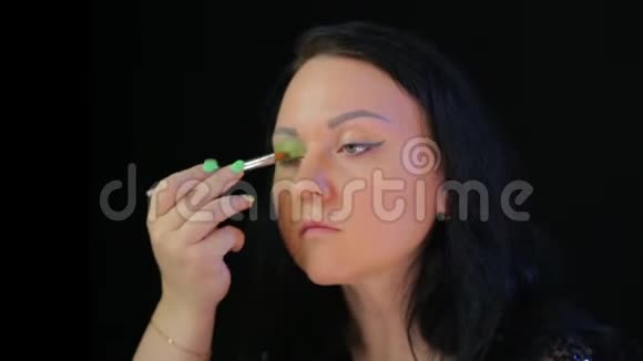 一个深色的女人在镜子前用绿色的阴影做眼妆视频的预览图