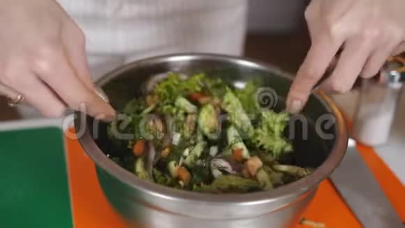 女人在沙拉里加盐在金属碗里加蔬菜视频的预览图