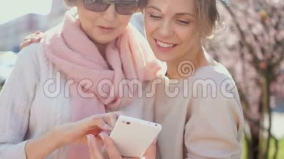 两个女人在智能手机里讨论照片公园里的春画像网络营销传销业务视频的预览图