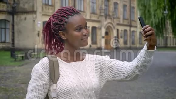 漂亮的非洲女学生拿着手机自拍女人拿着粉红色的可怕的背包站着视频的预览图