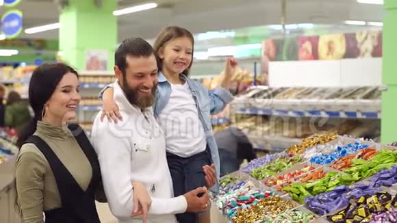 一位美丽的年轻母亲带着一个留着胡子的丈夫和一个可爱的女儿买糖果视频的预览图