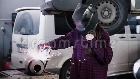 女孩电焊工穿格子衬衫和电焊工防护头盔的女孩在汽车上焊接金属视频的预览图
