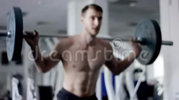 强壮的男人用杠铃在健身房里蹲着身体赤裸视频的预览图