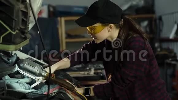 漂亮的女机械师深色头发穿着格子衬衫和帽子戴着防护眼镜修理汽车发动机概念视频的预览图