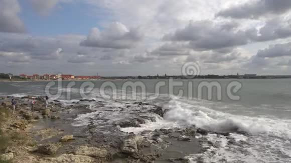 人们看着海浪海浪冲破海岸上的岩石视频的预览图