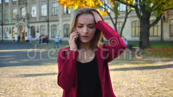 年轻女学生打电话听到坏消息站在大学外面不愉快的电话视频的预览图