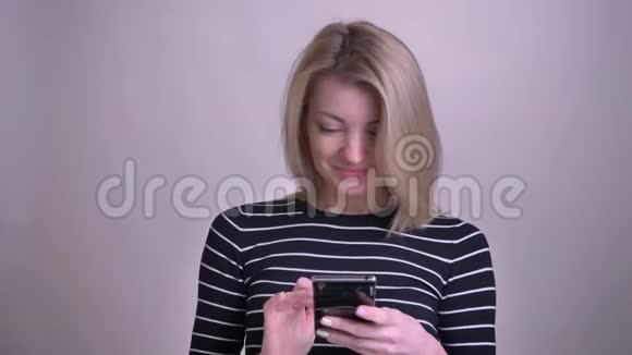 特写照片上的成年金发白种人女性在电话和看信息看着镜头微笑着视频的预览图