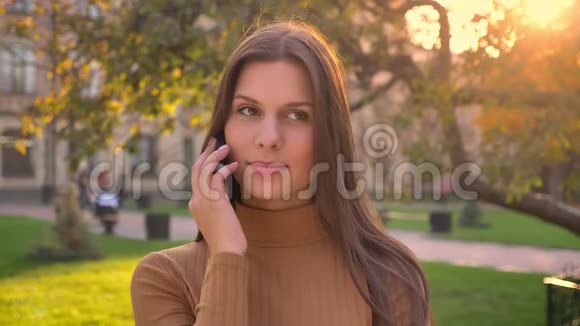 在绿色公园背景下漂亮的黑发女孩格尔在手机上说话的肖像视频的预览图