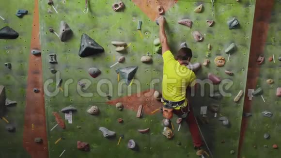 男性登山者爬上房间里的悬崖壁伸手抓住一个专业的集中登山者向上移动视频的预览图