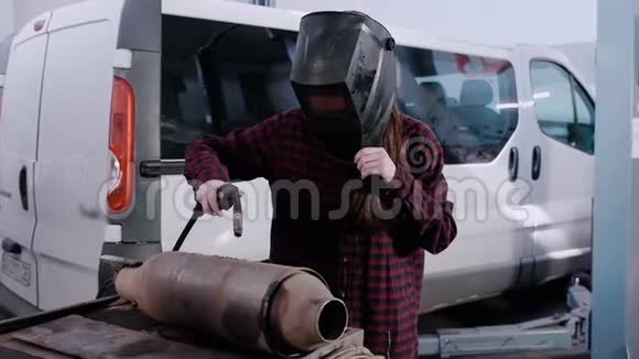 女孩电焊工穿格子衬衫和电焊工防护头盔的女孩在汽车上焊接金属视频的预览图