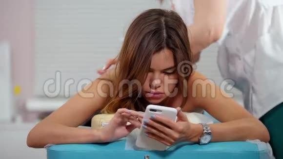 一位年轻的黑发女人正在接受放松的背部按摩坐在手机里看着屏幕视频的预览图