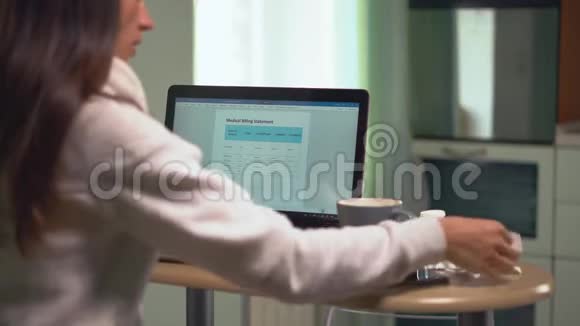 女人看着医疗账单在笔记本电脑上输入从账单到桌子的价格视频的预览图