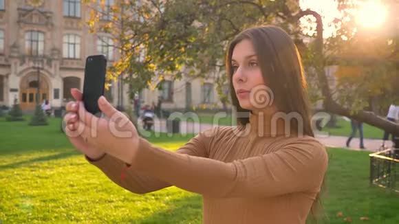 一幅美丽的黑发女孩在绿色公园背景下使用她的智能手机在视频聊天的肖像视频的预览图