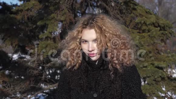 一个穿着黑色外套卷发的年轻女子在阳光明媚的冬日里洒下白雪视频的预览图