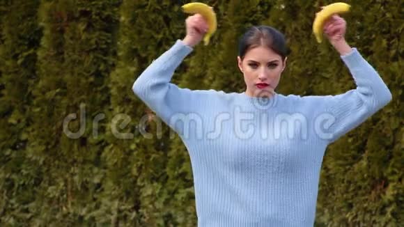 漂亮的年轻女人红唇穿着蓝色毛衣把香蕉放在头上像角一样模仿天使的小鬼视频的预览图
