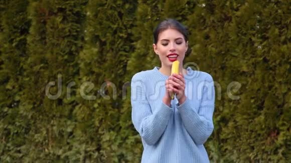 一位穿着蓝色夹克的迷人年轻女子举着香蕉当麦克风唱歌直视镜头视频的预览图