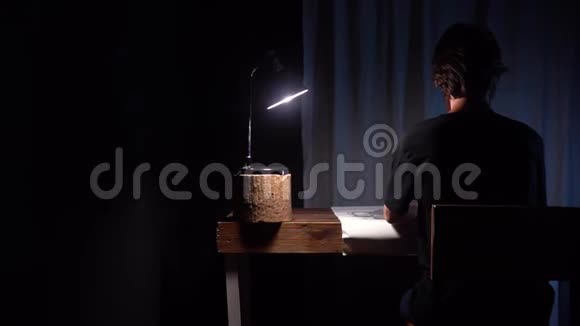 男子艺术家坐在桌子旁用纸和图案素描在黑暗艺术工作室与木制内部视频的预览图