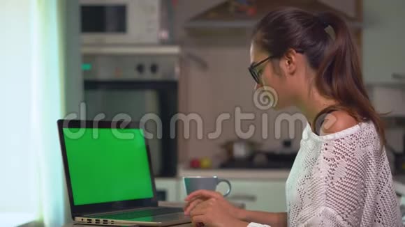 年轻的黑发女人在笔记本电脑上工作在家里上网学习绿色屏幕色度键视频的预览图