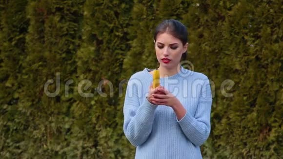 一位穿着蓝色夹克的漂亮年轻女子将香蕉放在他的耳朵上像打电话一样交谈视频的预览图