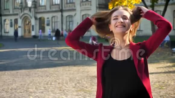年轻的女学生高兴地摇着头发笑着看着摄像机站在大学的背景上视频的预览图
