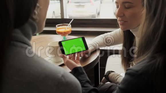 女朋友们看着智能手机上的绿色屏幕坐在咖啡馆里谈论它视频的预览图