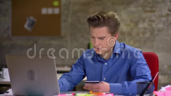 中年金发商人在办公室用信用卡和笔记本电脑支付smth的肖像视频的预览图