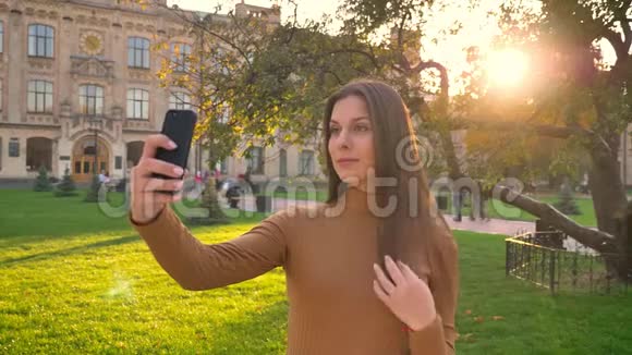 美丽的黑发美女在绿色公园背景下使用智能手机制作自拍照片的肖像视频的预览图