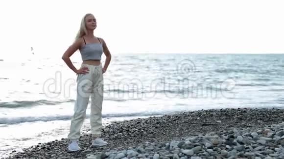 晨练训练前热身穿着运动服在海滩上做伸展运动的年轻女性视频的预览图