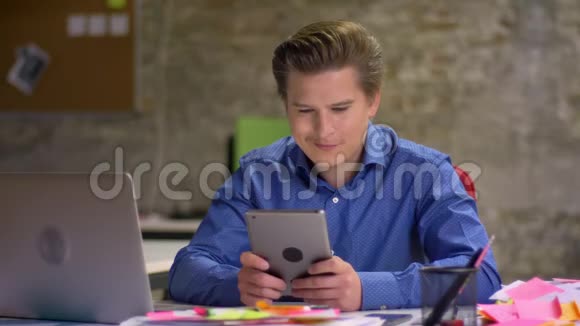 中年金发商人的肖像在办公室工作使用平板电脑满意和高兴视频的预览图