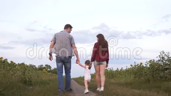 一家人带着一个小孩子走在路上笑在向日葵的田野旁孩子骑在父亲的怀里视频的预览图