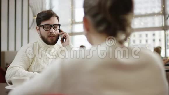 年轻的商人正和他的女朋友一起坐在餐馆的桌子旁谈论他的智能手机视频的预览图