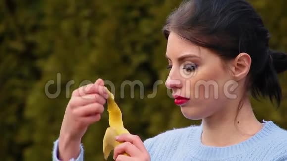 穿着蓝色夹克剥香蕉皮咬着香蕉留着深色头发和红唇的性感年轻女子视频的预览图