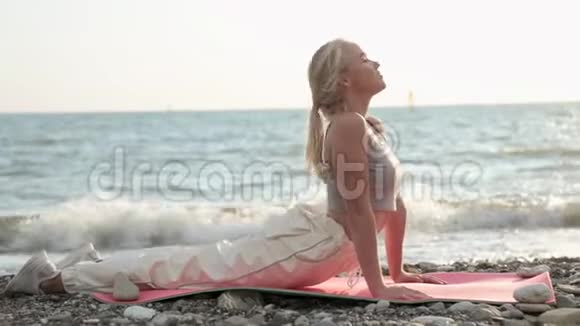 在夏季户外海边的沙滩上运动的年轻女子在瑜伽垫上伸展背部视频的预览图