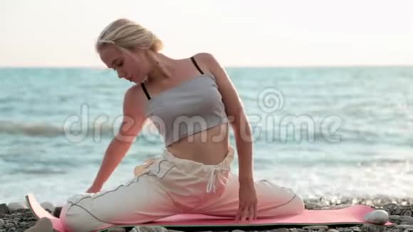 快乐的年轻健康的女人坐在沙滩上伸腿视频的预览图