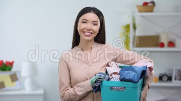微笑的年轻家庭主妇拿着篮子脏衣服洗衣服务视频的预览图
