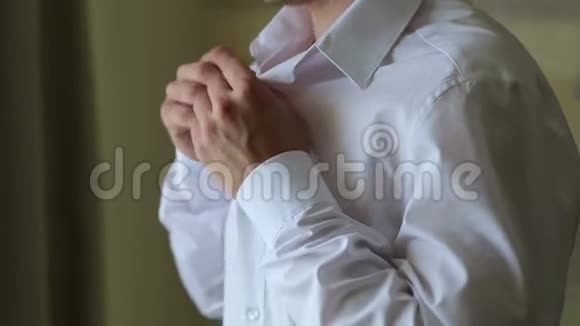 男人把他的白色衬衫扣在明亮的窗户前特写视频的预览图