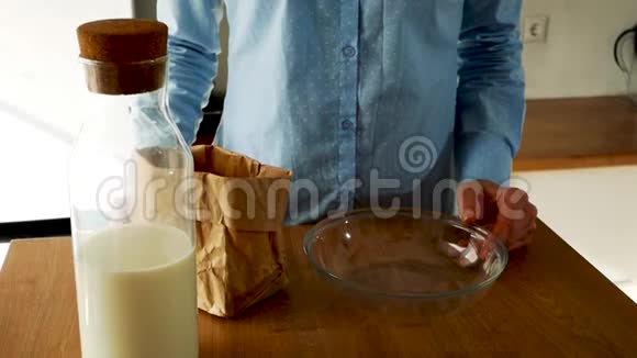 年轻女子把牛奶倒进厨房里的一碗玉米片里慢速视频视频的预览图