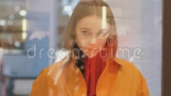 穿着橙色衬衫的年轻女子透过商店的玻璃看视频的预览图