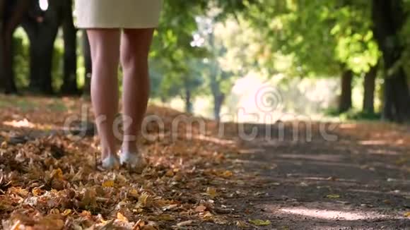 一个女孩在公园里散步和踢落叶优雅的女人穿白色短裤金秋概念视频的预览图
